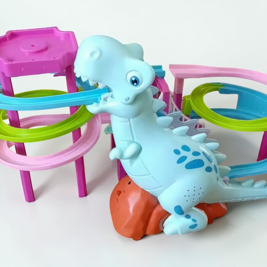 A light blue dinosaur toy with blue paw-print spots sits on an orange rock, interacting with a pink, purple, green, and blue marble run track set on a white background.